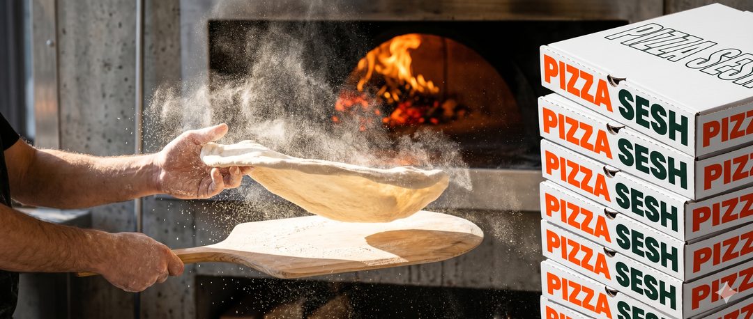 Pizzaiolo stretching dough on a peel in a cloud of flour, glowing wood fire behind